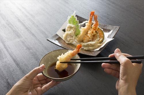 天ぷらを天つゆにつけて食べようとしているところの写真