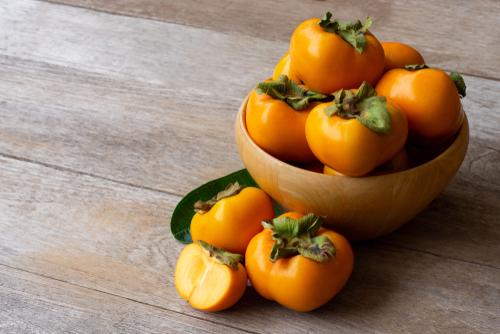 古い木製のテーブルの背景に分離されたスライスと木製のボウルに柿の果実のための新鮮なオレンジ色の有機熟した柿