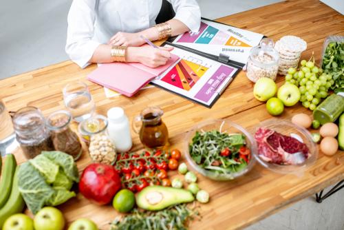 栄養士がダイエット計画を作成し、健康的な食事のトピックに関するさまざまな健康的な製品と図面をテーブルの上から見た