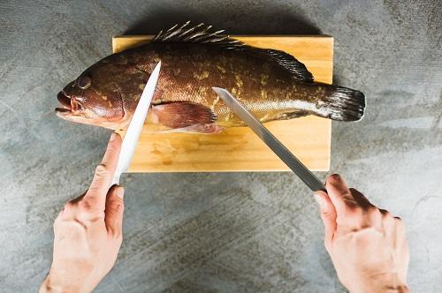 2本のナイフで木の板に大きなグルーパーの魚を切る