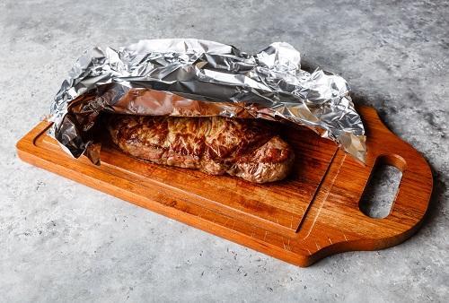 アルミホイルで覆われた木の板で休む焼きステーキ