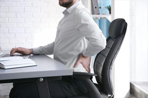 オフィスで作業中に背中の痛みに苦しんでいる男性