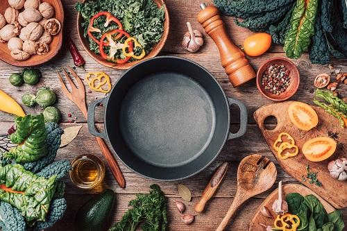 さまざまな有機野菜の材料と空の鉄の調理鍋、木製のボウル、木製の背景のスプーン
