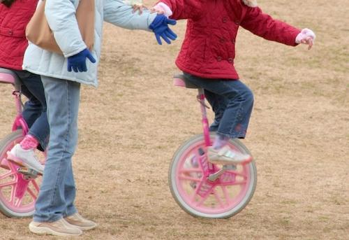 母親に支えてもらいながら一輪車の練習をする子供の写真