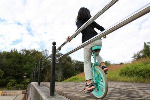 手すりにつかまりながら一輪車の練習をする子供の写真