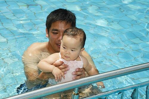 パパに抱っこされてプールに入る子どもの写真