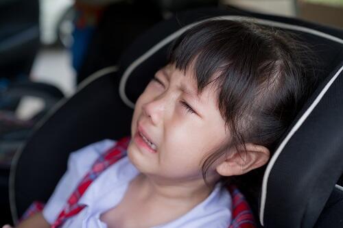 助手席で泣いているジュニアシートに座った女児のイメージ写真