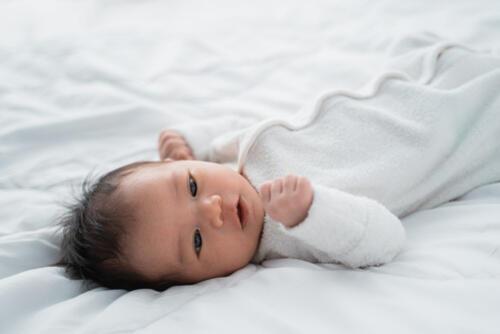 ベッドに横になりながら遠くを見つめる赤ちゃんの写真