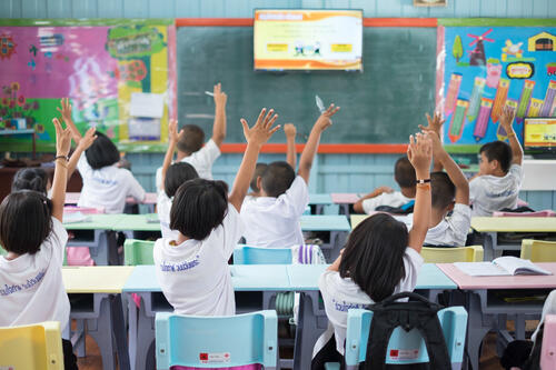 学校の教室で元気よく手を挙げる子どもたちの写真