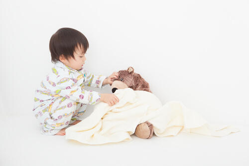 ぬいぐるみにお布団をかけてあげるパジャマ姿の赤ちゃんの写真
