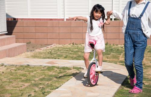 子供の一輪車の練習をサポートしながらコミュニケーションをとる母親のイメージ写真