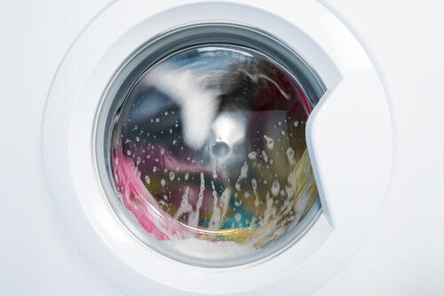 泡立てて回転する洗濯中のドラム式洗濯機の写真