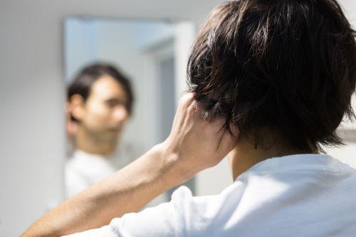 鏡で髪型をチェックする耳掛けヘアの男性の写真