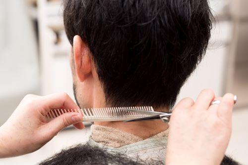 ハサミで後ろをカットしてもらっているマッシュヘアの男性のイメージ写真