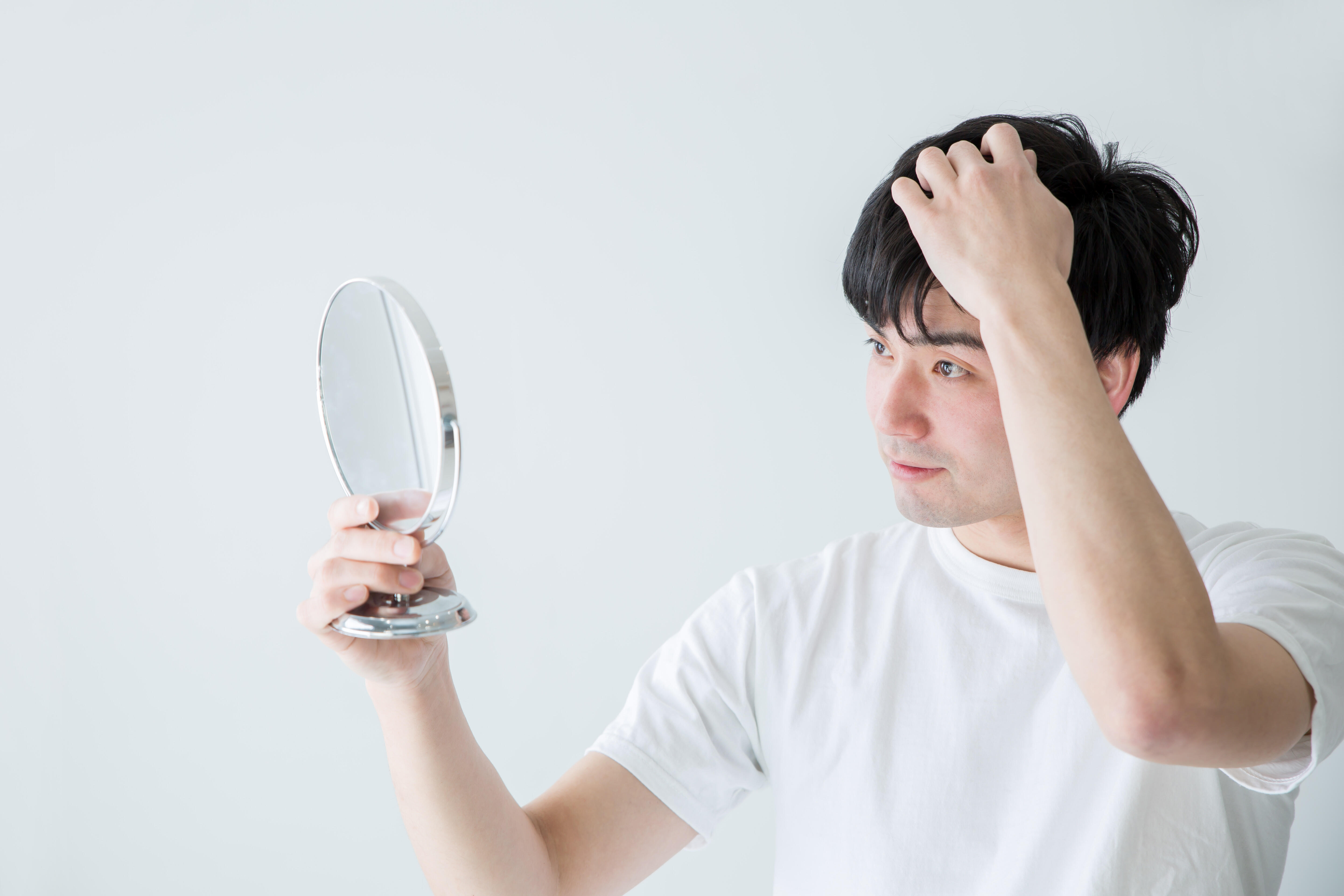 鏡を見ながら髪の毛をいじる男性の写真