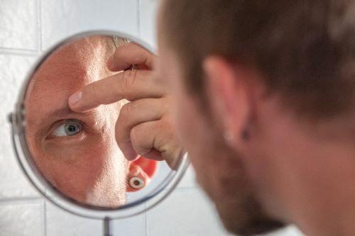 鏡を見ながら自分の眉毛に指を当てる男性の写真