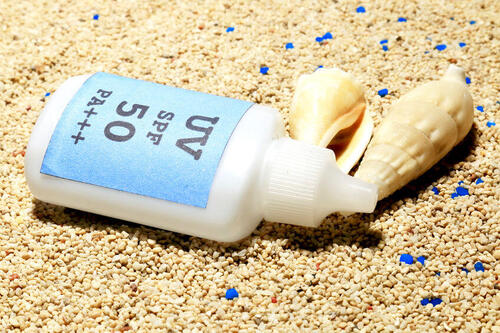 砂浜と貝殻、ボトルに入った日焼け止めの写真