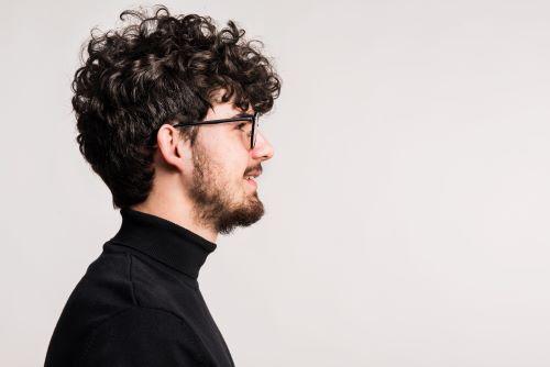 「オシャレなヘアスタイルをした、横を向いている天パの男性」のイメージ写真