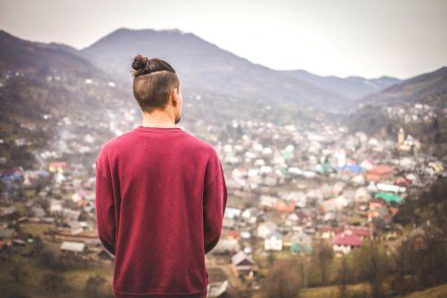 小高い丘から街を眺めるマンバンヘアの男性の後ろ姿の写真