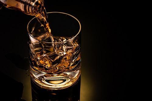 氷を入れたグラスにウイスキーを注いでいる写真